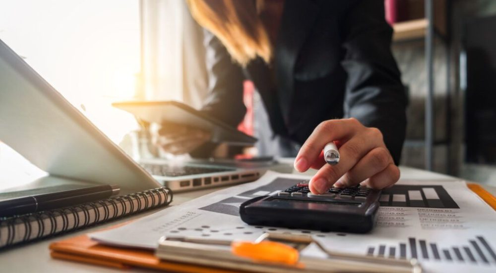 Businesswoman,Calculates,Financials,With,Graph,Paper,On,The,Table,On