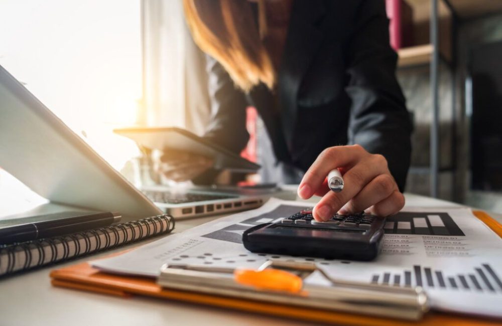 Businesswoman,Calculates,Financials,With,Graph,Paper,On,The,Table,On