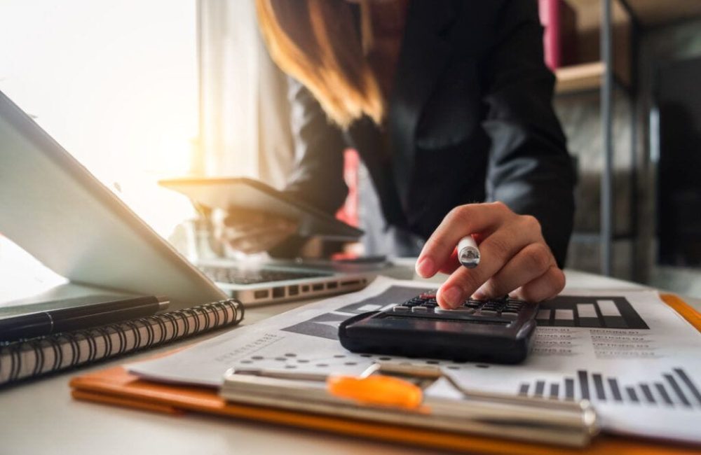 Businesswoman,Calculates,Financials,With,Graph,Paper,On,The,Table,On